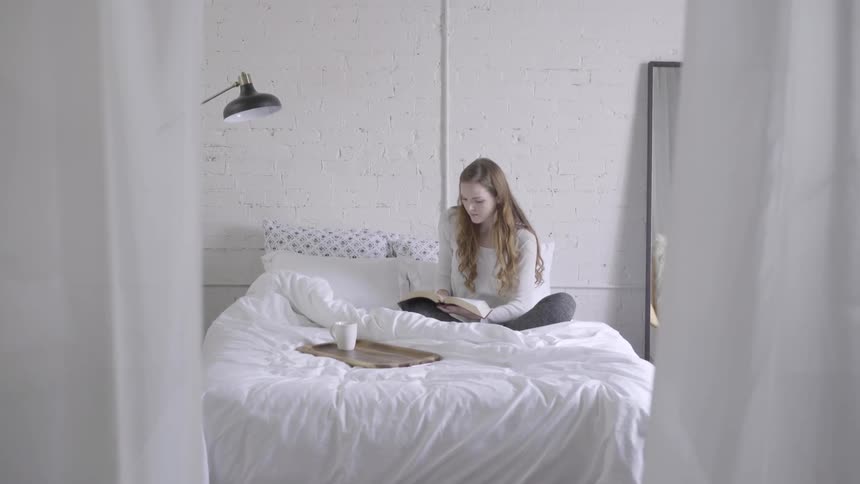 A teenager sitting on her bed reading a book