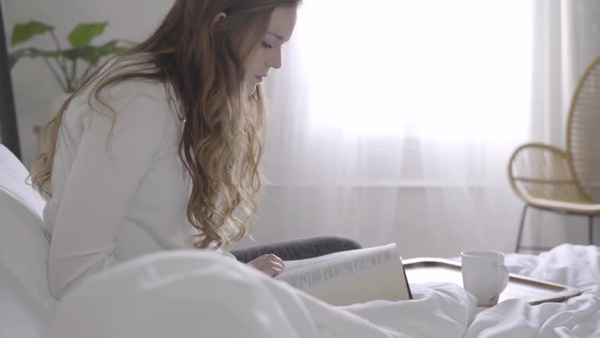 A woman with long hair sitting in her bed closes a bible shes been reading