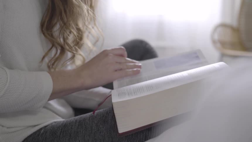 A woman turns the pages of a thick book she has on her lap