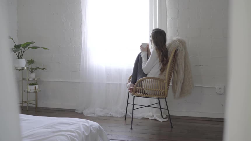 A woman sits in a chair by a window