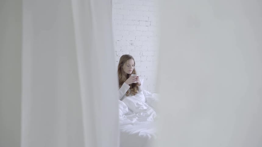 A woman smells a drink while sitting in bed