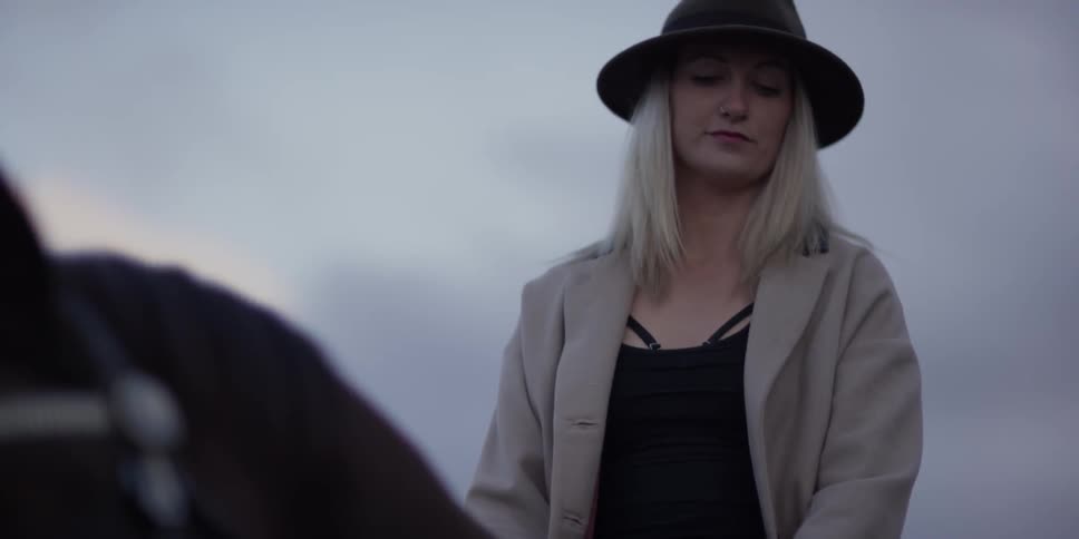 A young woman wearing a hat rides a horse at dusk