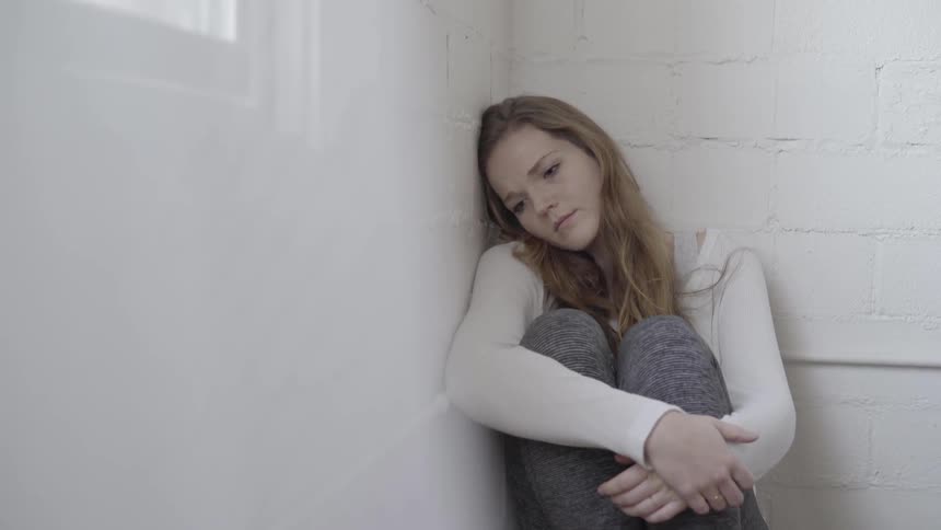 A woman sitting in the corner with her head against the wall