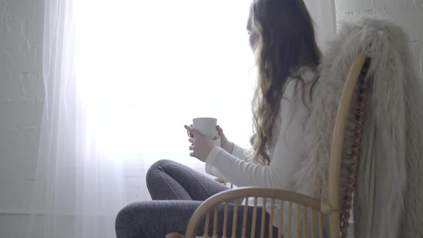 A woman is sitting by the window with a cup