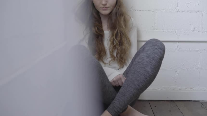 Female with long hair sitting cross legged in a corner of the room