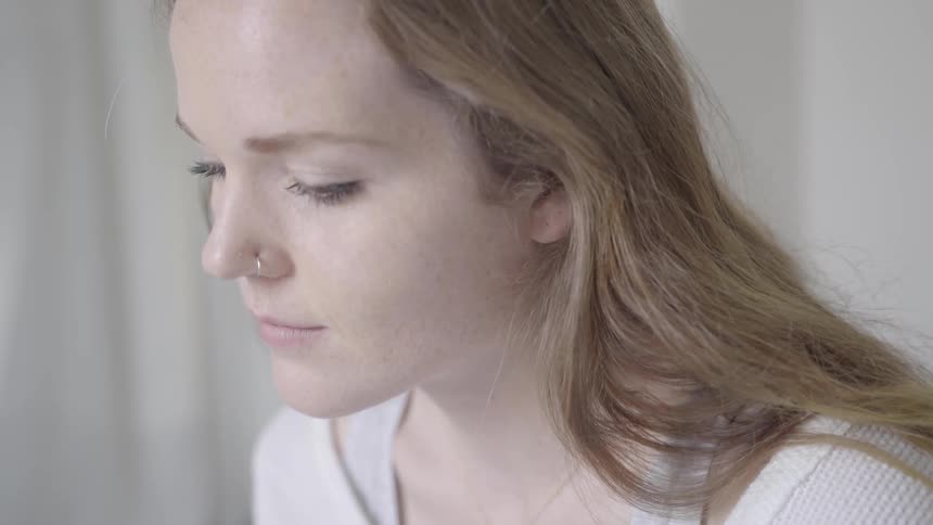 A woman with long hair and a nose ring looks down and blinks
