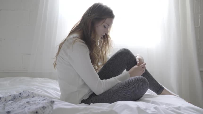 A woman sitting on a bed in a bright room
