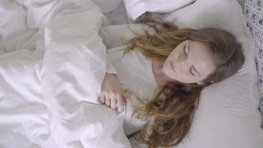 A woman with long hair sleeps on a bed with white sheets and her hair spread out