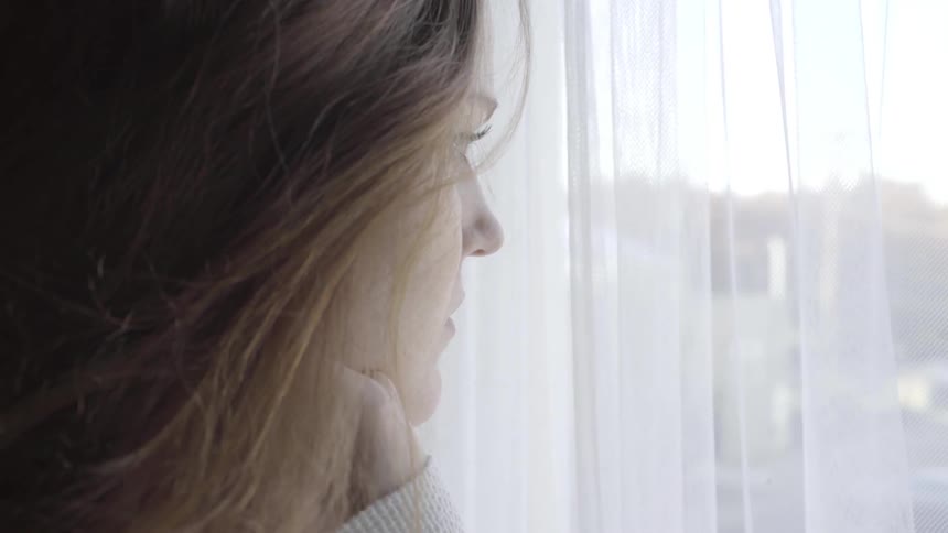 A woman stares out of a window and blinks her eyes