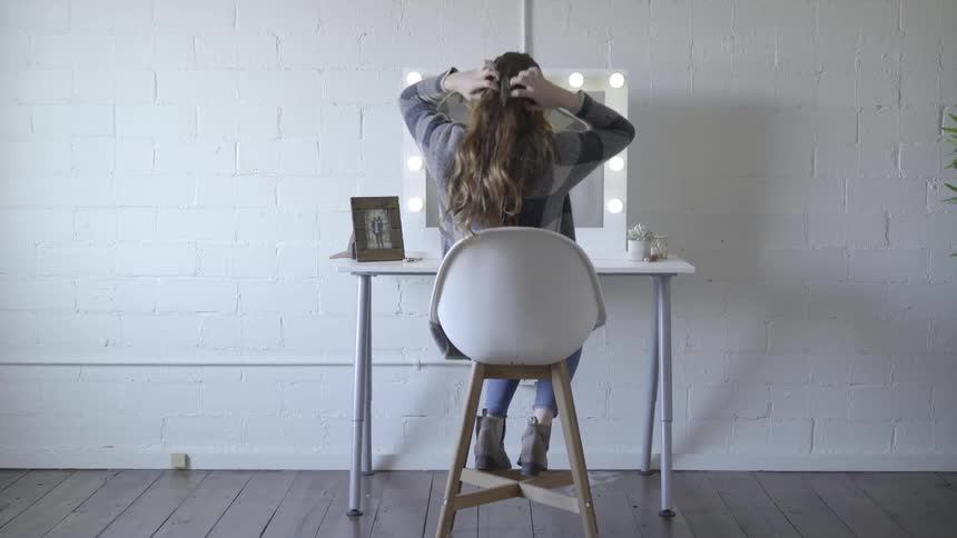 A woman fixes her hair in front of a mirror
