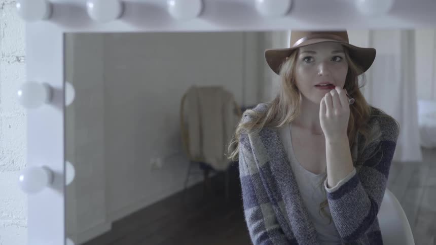 Woman applying lipstick in front of a mirror