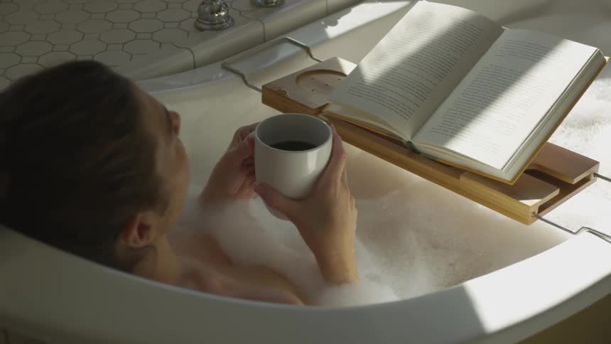 A woman is drinking coffee in a bathtub while reading