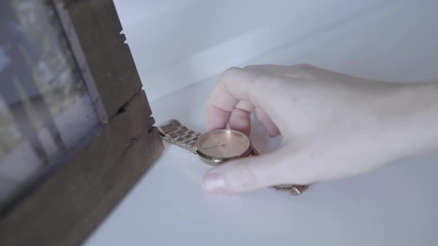 A person picks up a watch from next to a picture