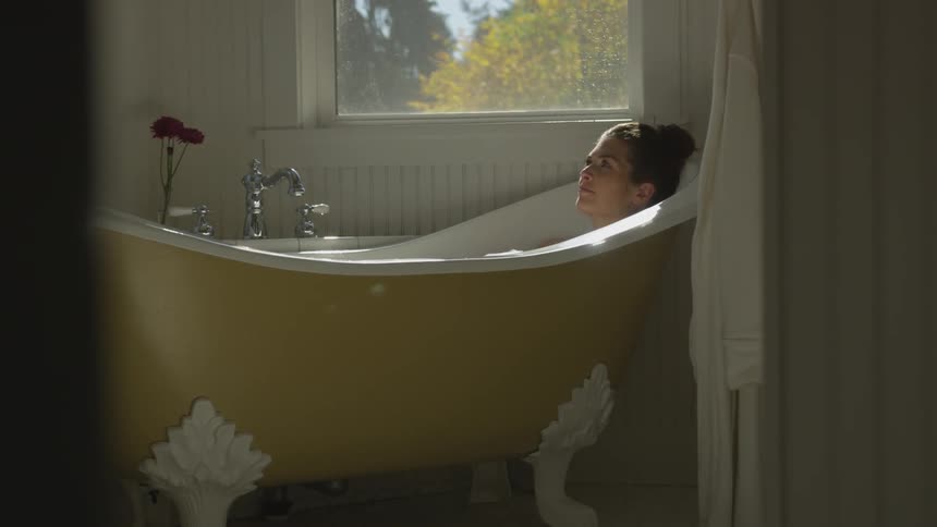 Woman relaxing in a yellow vintage bathtub taking a bath