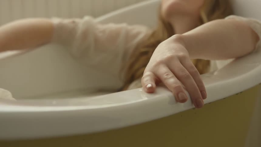 A young woman is reclined inside a bathtub while wearing a nightgown