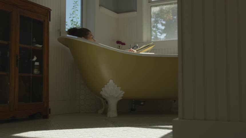 Woman reads book in antique claw foot bathtub
