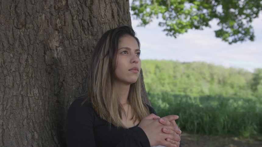Blonde woman sitting against a tree in the country reflecting on life
