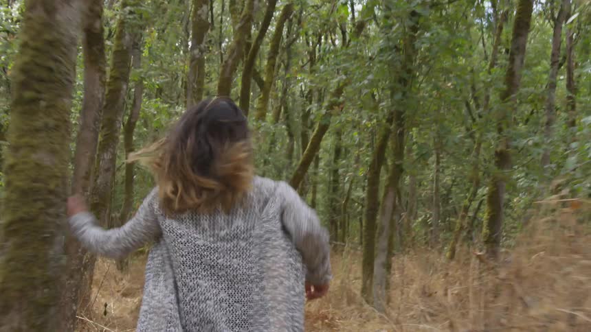 Woman runs away from camera through underbrush in forest