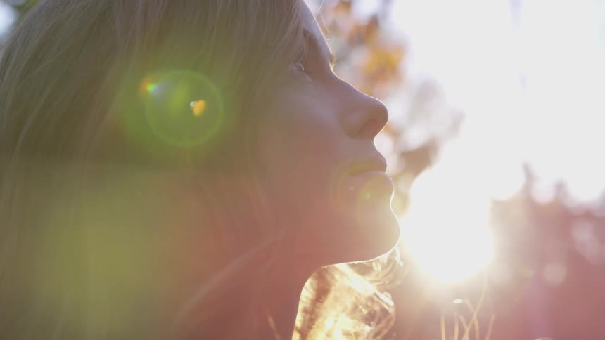A young woman is l looking upwards pensively in a grove of trees while the sunlight shines on her