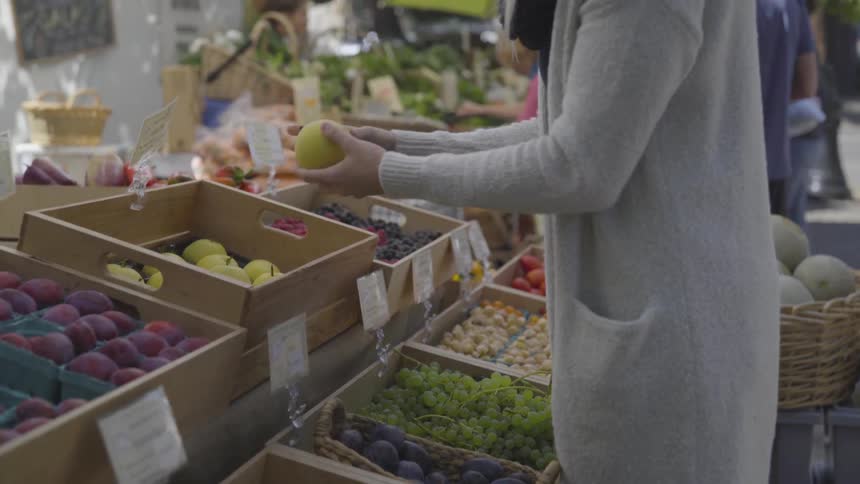 Woman picks fruits on a stand in a street market