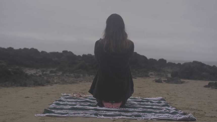 A woman taking photos while kneeling on a blanket on the beach