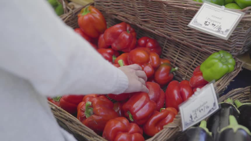 A woman chooses a red bell pepper from a basket