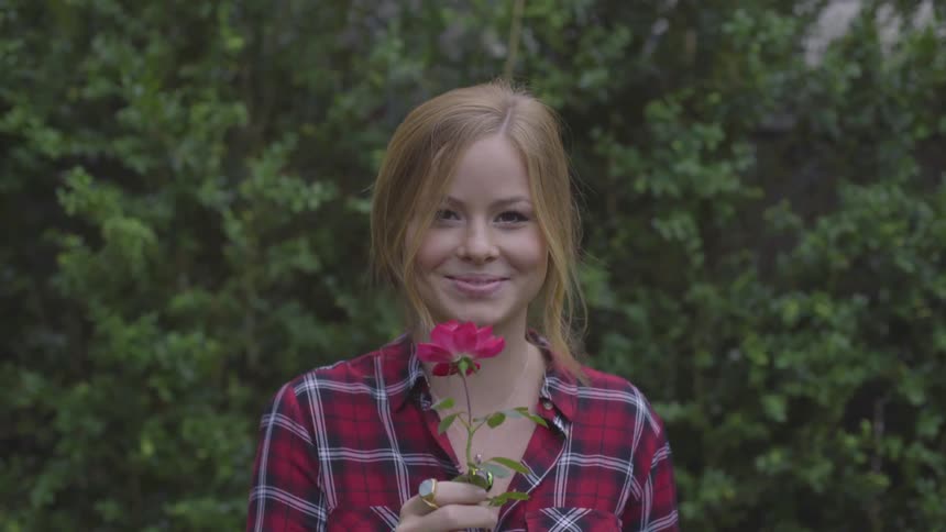 A young blonde female sniffs a red rose and smiles