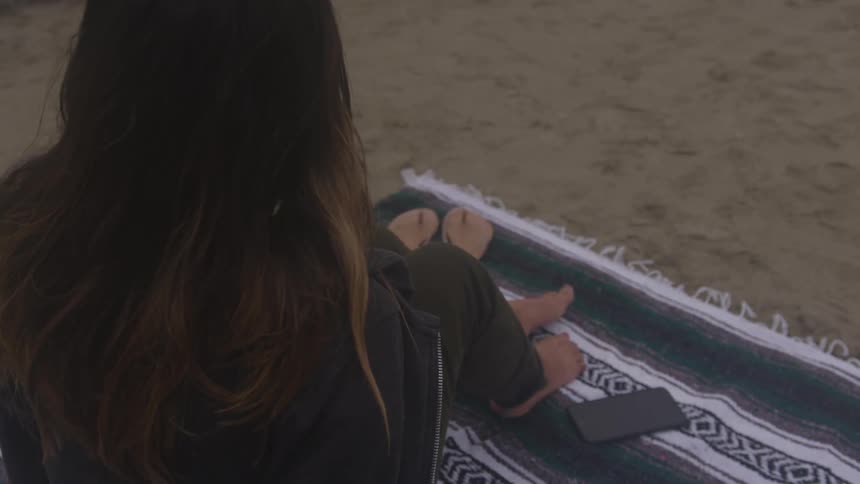 A woman sitting on a beach towel on a beach