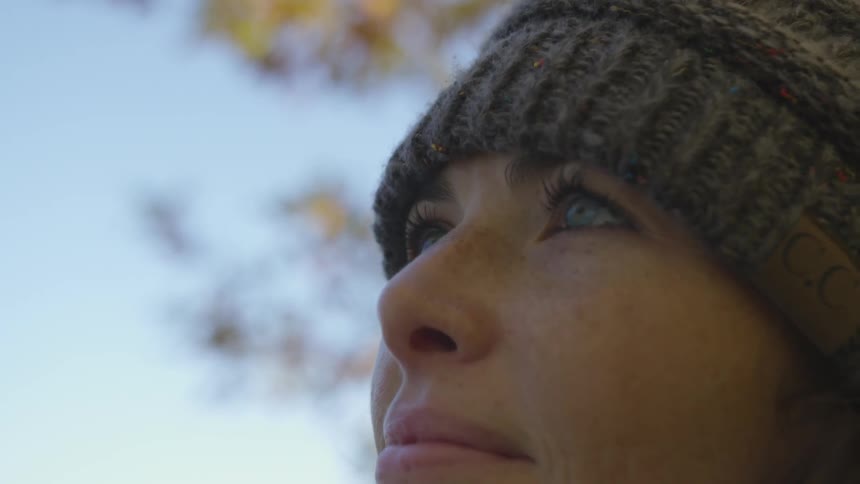 A white woman with blue eyes and wearing a knit cap stares upwards