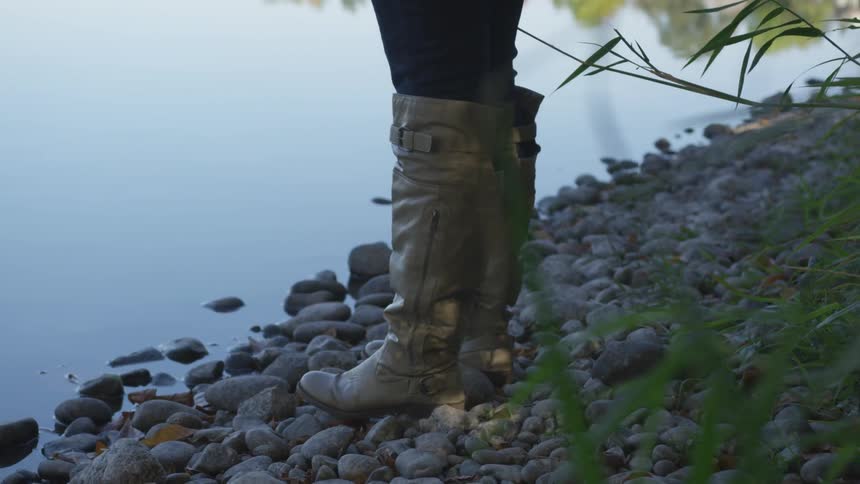 A woman in boots standing on pebbles by the shore