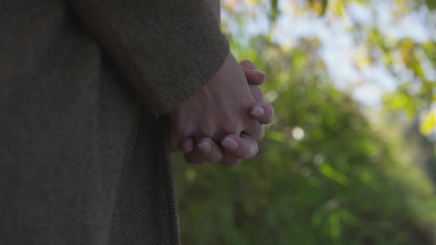 A white person stands still with clasped hands