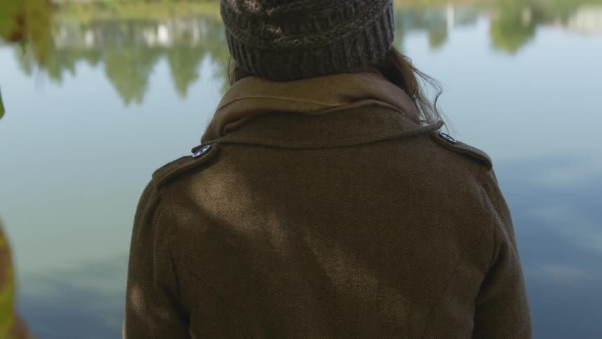 A woman sits by a lake