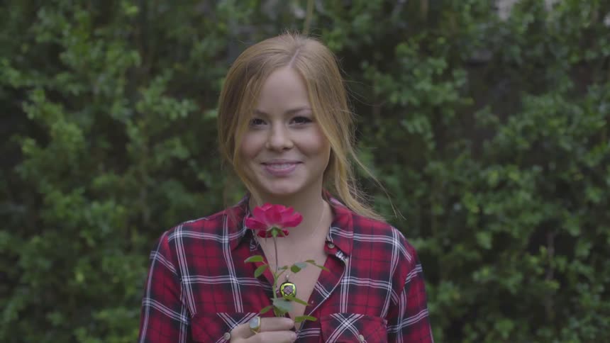 A young white teenager smells a flower and smiles