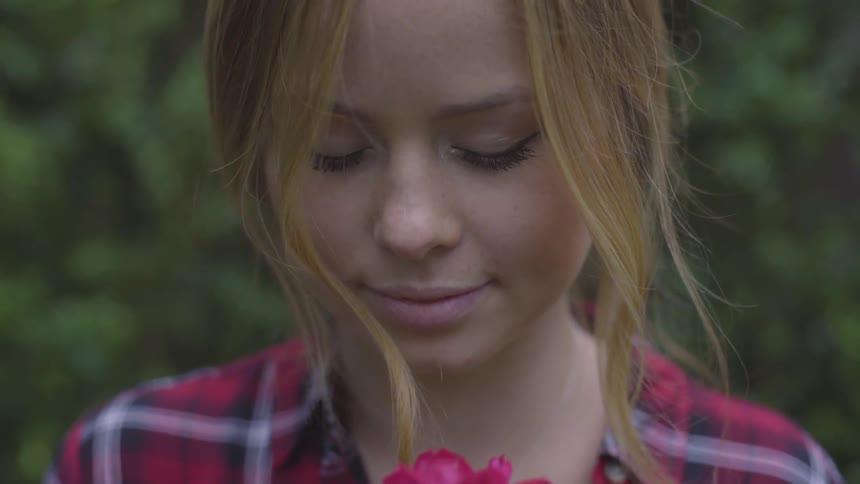 A young woman with fair hair sniffs a rose and smiles