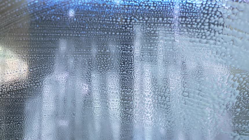 A person cleans a windshield and the soap drips down
