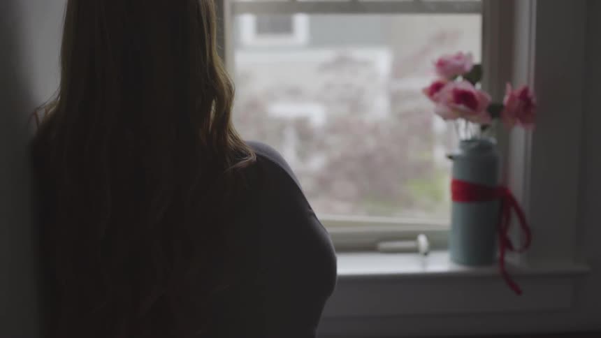 A young woman stands looking out the window