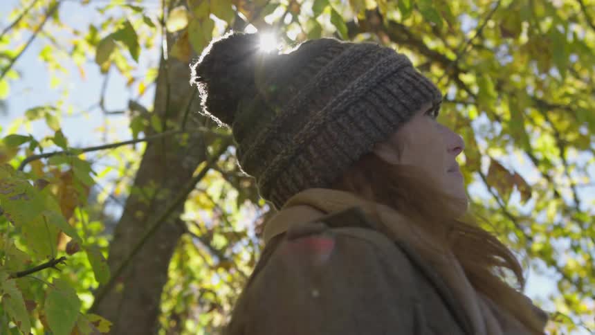 Woman stands outdoors in knit cap looking at sky