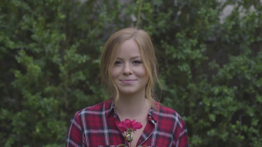 A young woman with fair hair sniffs a rose and smiles
