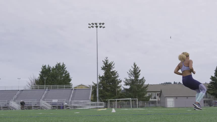 A woman sprints back and forth on a soccer field