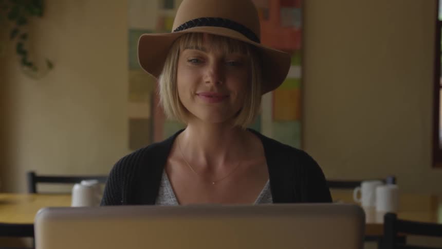 A woman sitting in an empty restaurant smiles as she works on her laptop