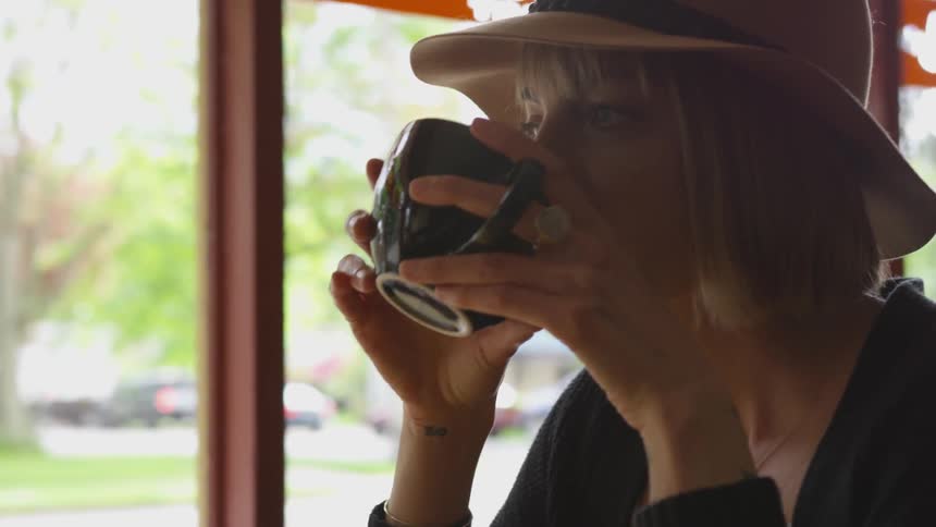 A blonde haired female drinking from a mug in a diner
