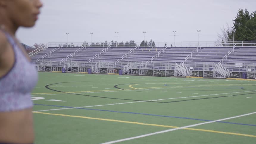 A woman bent over with her hands on knees catching her breath on an empty athletic field