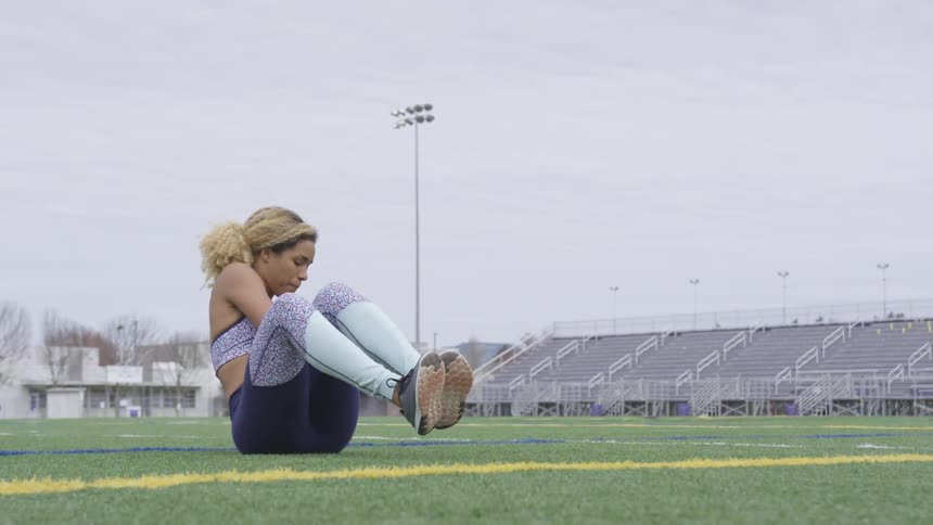 A black athlete in workout attire stretches on stadium grass