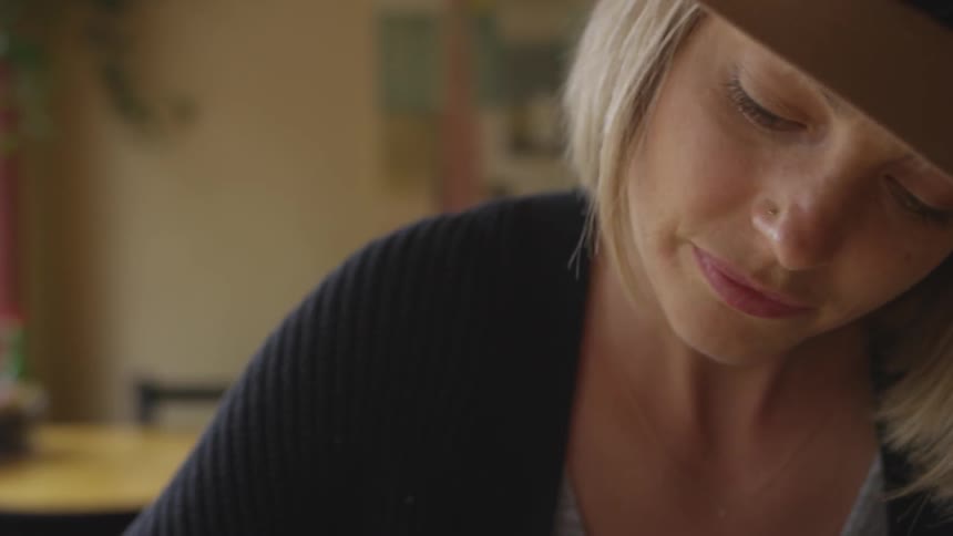 A woman with blonde hair and wearing a hat sits and concentrates on something that she is working on