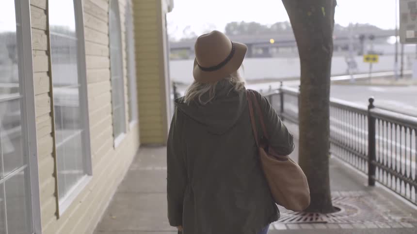 A woman wearing a coat and a hat and carrying a purse is walking around and looking at everything