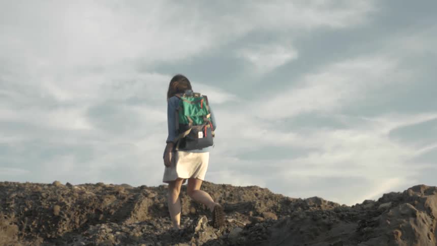 A woman with a backpack is walking up a rock ledge