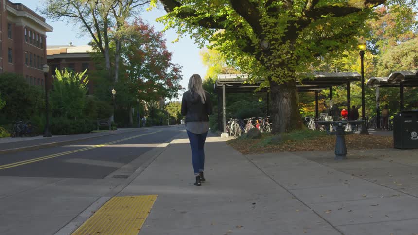 Woman walking down a city street near a park