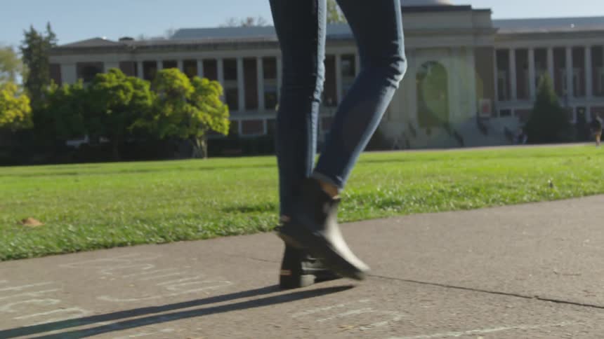 A woman with boots and jeans walking on campus