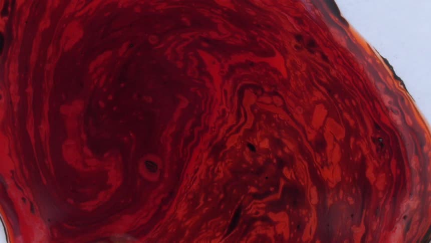 A liquid in shades of red swirl in a container