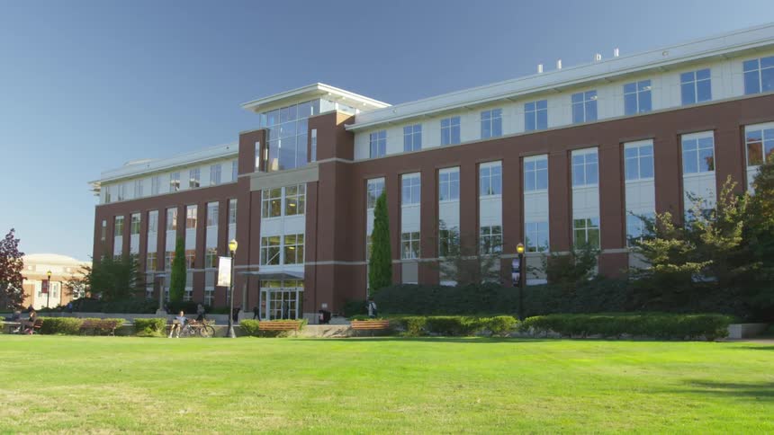 Students walk and sit in front of a college building